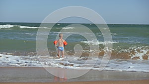 Boy runs into the sea. Waves wash over the beach. Child in armbands on vacation at sea. The child dives into the raging