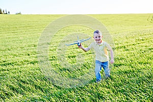 Boy runs with toy airplane in summer through field. Happy child running and playing with toy airplane outdoors. Boy dreams of