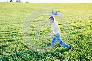 Boy runs with toy airplane in summer through field. Happy child running and playing with toy airplane outdoors. Boy dreams of