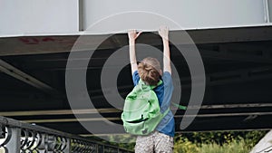 The boy runs under the bridge and jumping grabs hands over the bridge. Active sports boy.