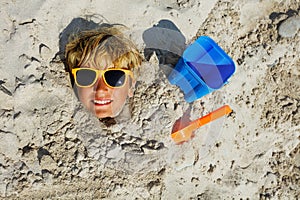 Boy's face in sunglasses dug into sand at beach view from top