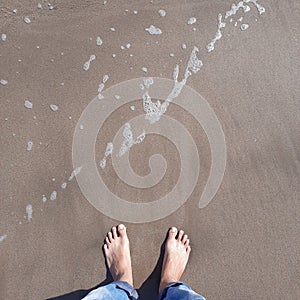 boy's feet standing on grey sandy beach with sea wave