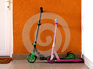 Boy and girl small colorful scooter leaning against the stucco wall next to white entrance door