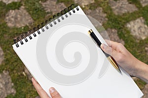 Boy`s hand with a pencil over an open notepad in the park