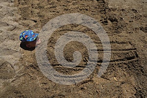 The boy's head peeks out of the sand, the body is buried in the sand, summer fun on the beach. Cute boy burried in