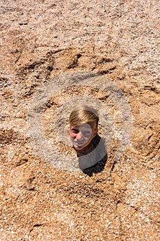 The boy`s head is sticking out of the sand