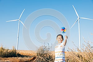 Boy& x27;s playful fascination near wind turbines holding a pinwheel toy