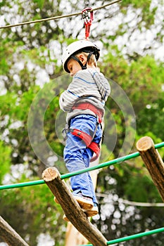 Boy in safe equipment on the rope-ladder in adrenalin park
