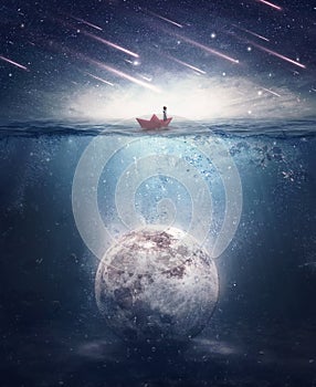 Boy sailing in a paper boat searching for the moon sunken underwater. Satellite drowned in the ocean water in a mysterious night