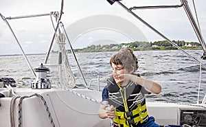 Boy sailing pulling ropes to adjust sails on sailboat