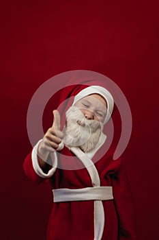 A boy in a Santa Claus costume holds his thumbs up.