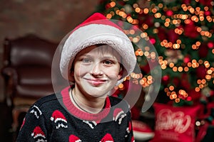 A boy in Santa Claus hat in the background of the lights of the Christmas tree. Christmas Eve, a boy waiting for gifts