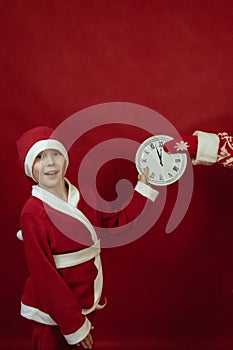 A boy in a Santa costume holds a white watch on a red background.