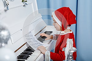 Boy in santa costume. Kid concept for merry Christmas and happy new year celebration. Small boy enjoys playing piano for