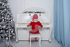 Boy in santa costume. Kid concept for merry Christmas and happy new year celebration. Small boy enjoys playing piano for