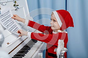 Boy in santa costume. Kid concept for merry Christmas and happy new year celebration. Small boy enjoys playing piano for