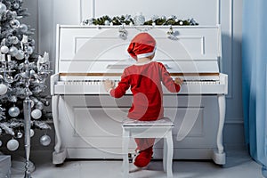 Boy in santa costume. Kid concept for merry Christmas and happy new year celebration. Small boy enjoys playing piano for