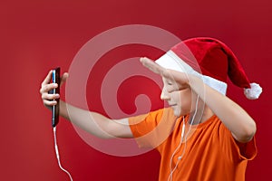 A boy in a Santa hat holds a phone in front of him and shouts cheerfully