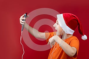 A boy in a Santa hat holds a phone in front of him and shouts cheerfully