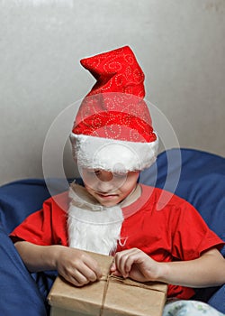 A boy in a Santa hat unties the rope on the gift box, focus on the hands. Portrait