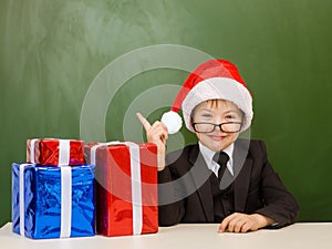 Boy in Santa red hat points on empty green chalkboard