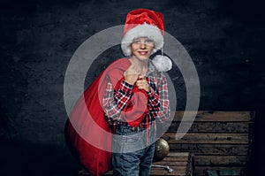 A boy in Santa`s hat holds New Year gift sack.