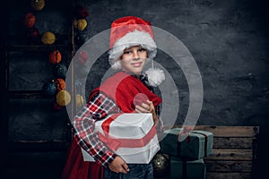 A boy in Santa`s hat holds New Year gift sack.