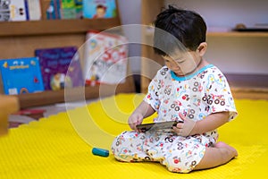 Boy sat down and looked at the mobile phone on the yellow floor.