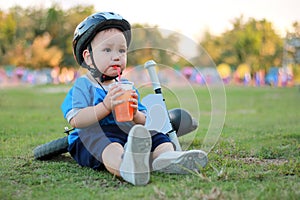 The boy sat and drank water on the lawn beside the bike.