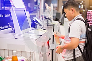 The boy is scanning the product at the automatic payment machine.