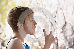 Boy of school age in breathing mask inhaler on a background of flowering trees. Home treatment. Prevention