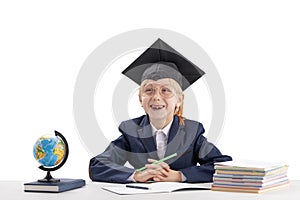 Boy in school uniform and students hat sits at desk and laughs on white background. Education in university college abroad