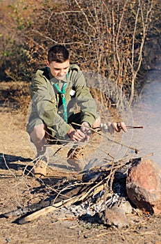 Boy Scout Cooking Sausages on Stick over Campfire