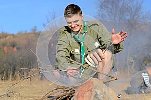 Boy Scout Cooking Sausages on Stick over Campfire