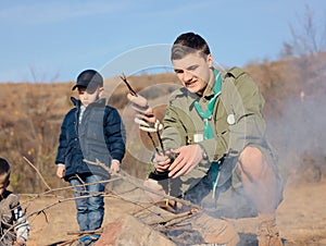 Boy Scout Cooking Sausages on Stick over Campfire