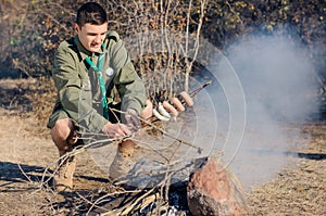 Boy Scout Cooking Sausages on Stick over Campfire