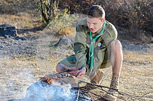 Boy Scout Cooking Sausages on Sticks over Campfire