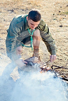 Boy Scout Cooking Sausages on Sticks over Campfire