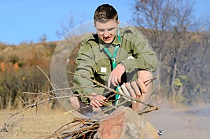 Boy Scout Cooking Sausages on Sticks over Campfire