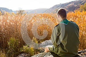 Boy Scout Sitting on the Rock Watching Brown Field