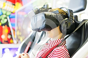 Boy screaming, wearing virtual reality gogglesplay games, siting in 4D chair. Surprised. Child experiencing 4D gadget