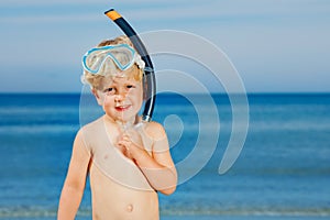 Boy with scuba mask fins stand on a beach ready to dive in sea