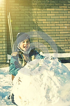 boy sculpt a snowman in the backyard of the house clear winter day. The boy rolls a snowball to build a snowman in the