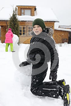Boy sculpts snowman near wooden country house photo
