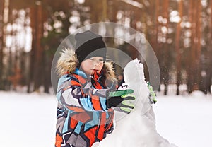 Boy sculpts snowman in winter in the woods on a sunny day