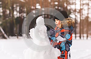 Boy sculpts snowman in winter in the woods on a sunny day