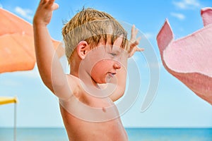 A boy at the sea on the beach among sun umbrellas spread his hands to the sides