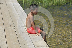 Boy seating on a wooden foot bridge on a lake