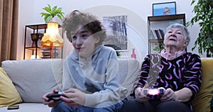 Boy and senior women playing video game on console. Grandmother and grandson playing video games using gamepads at home