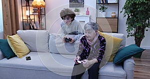 Boy and senior women playing video game on console. Grandmother and grandson playing video games using gamepads at home